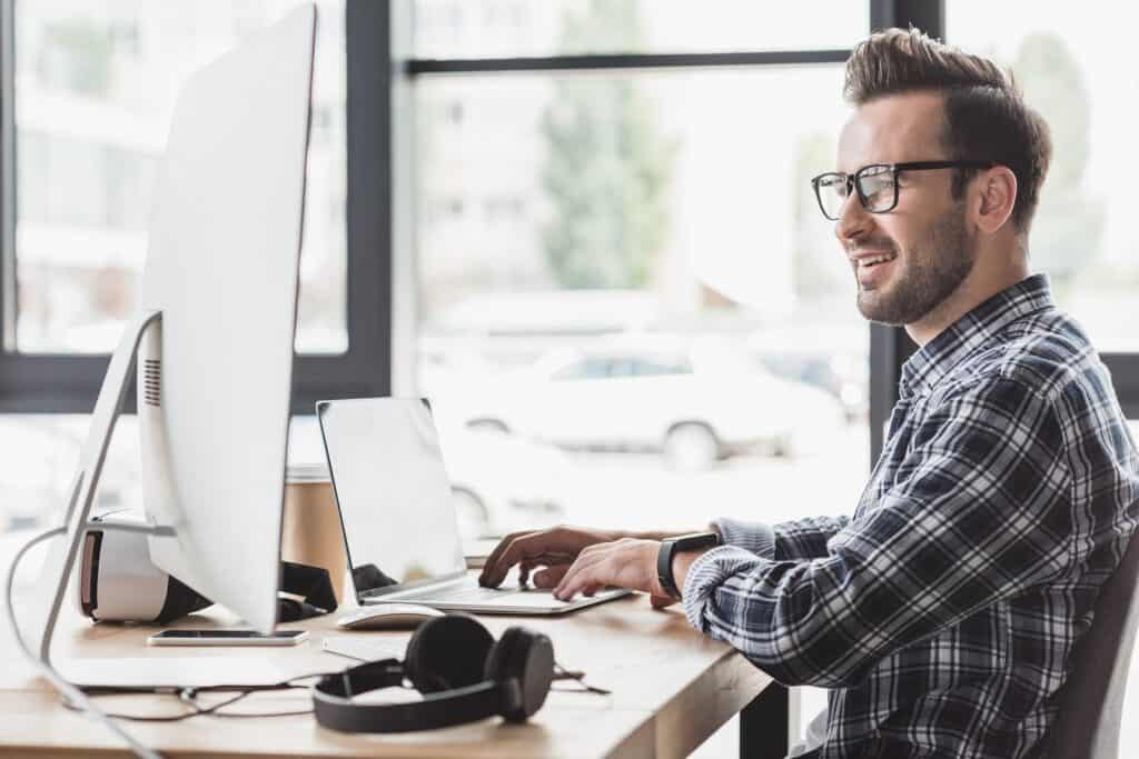 smiling man editing videos on a laptop and desktop